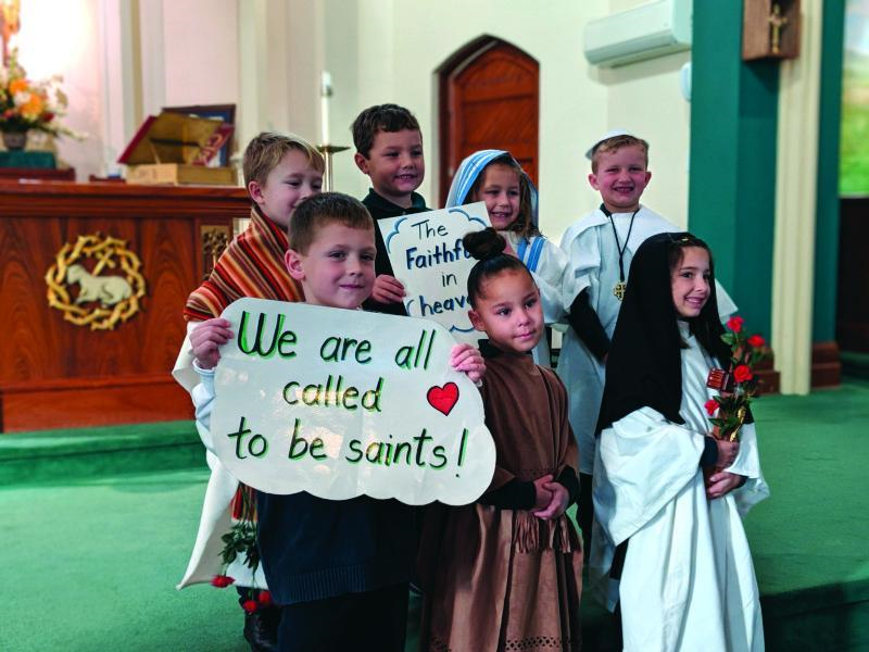 2022 Archbishop's Annual Appeal. Young students at the alter. One holding a sign that reads, 'We are all called to be saints.'